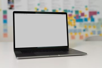 A laptop on a white table with a blurred background featuring colorful note papers.