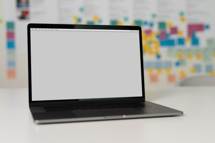 A laptop on a white table with a blurred background featuring colorful note papers.